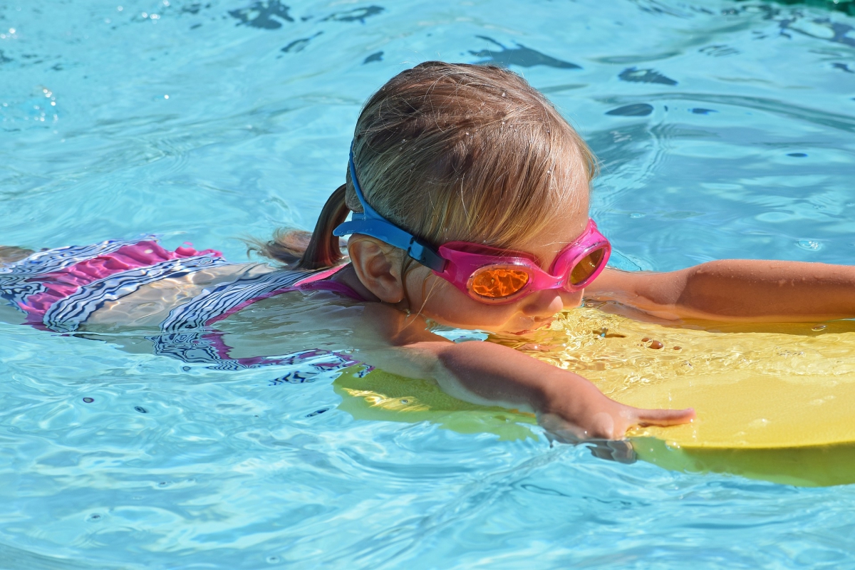 niña nadando con una tabla en una piscina en verano